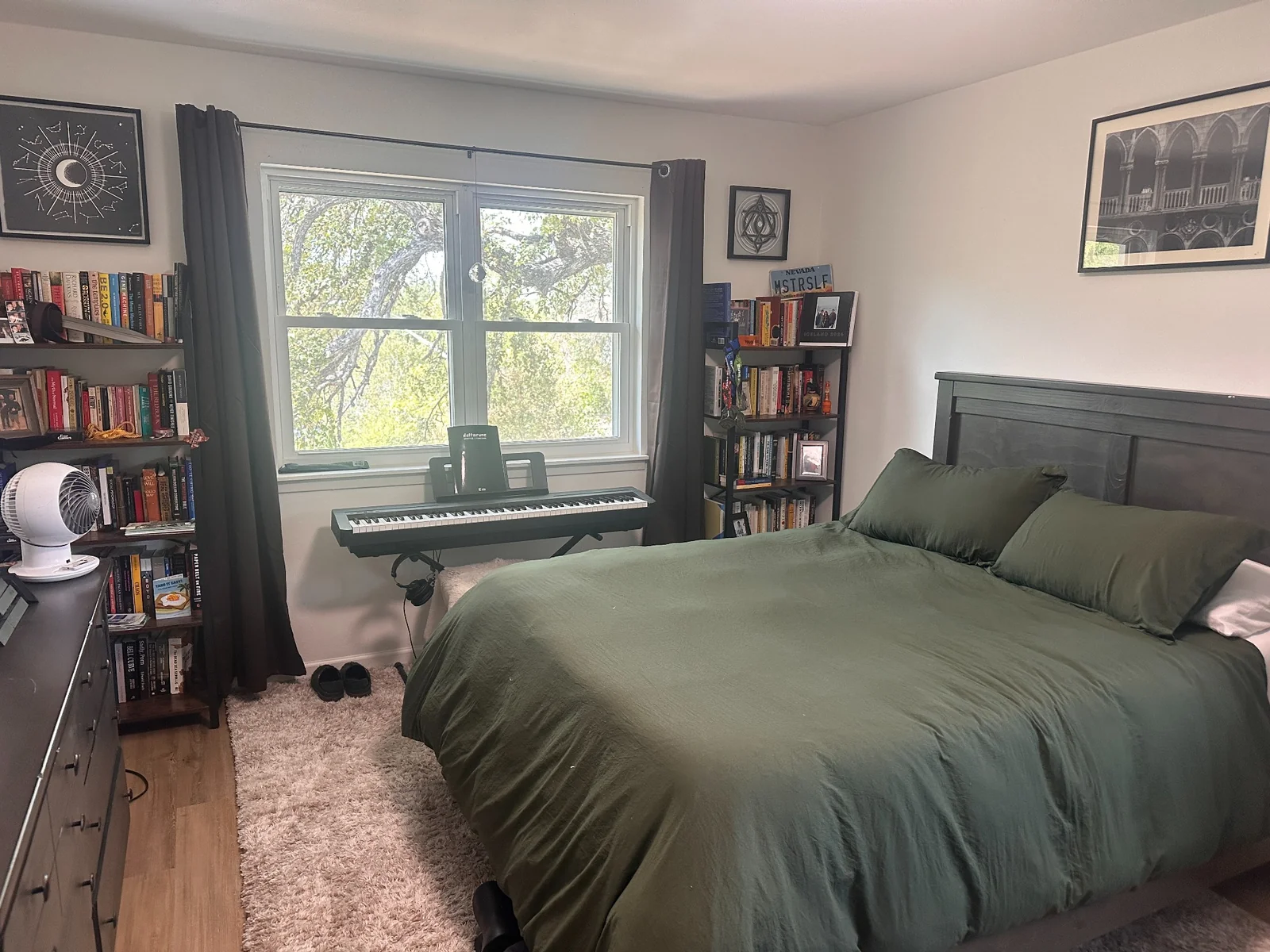 Bedroom with green bedding, bookshelves, and a keyboard beneath the window