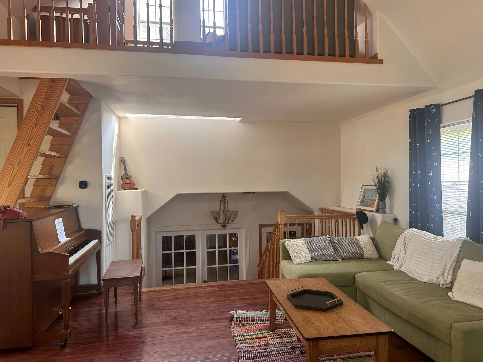 Conservatory with a green sofa, upright piano, wooden stairs, and an open loft above