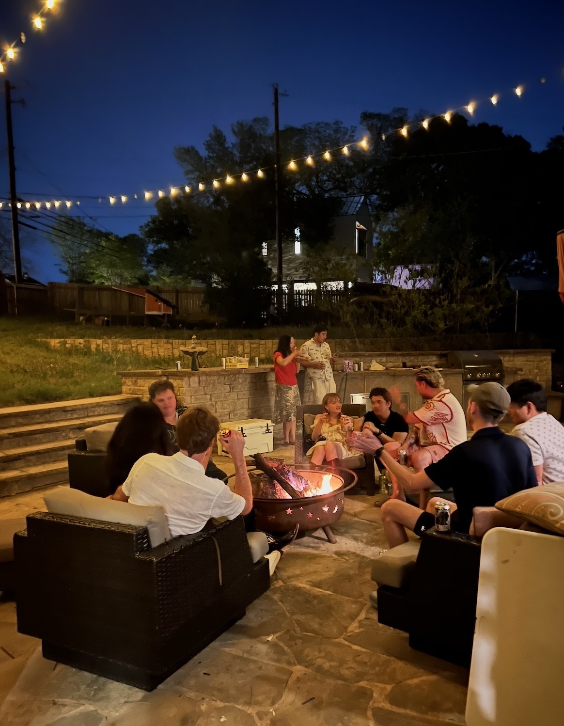 Friends gathered around the fire pit under string lights at night