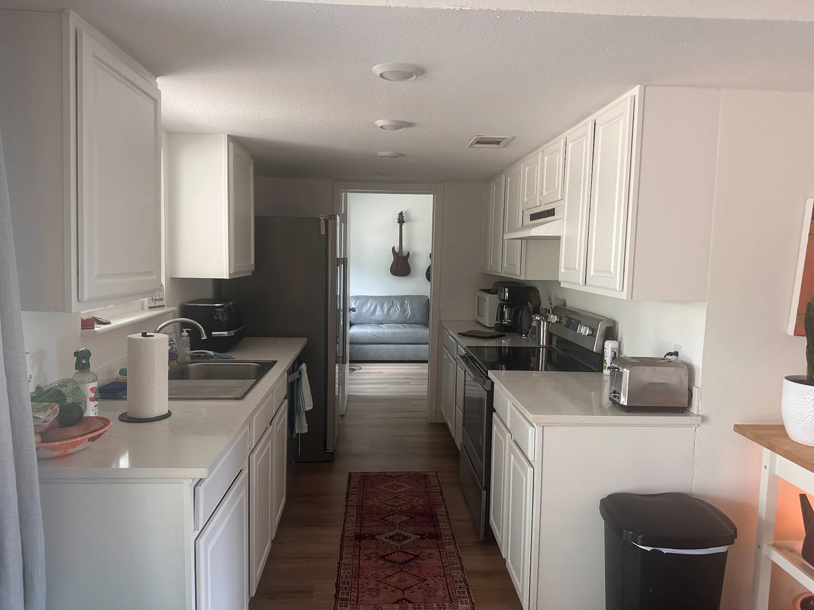 Galley kitchen with white cabinets, stainless steel appliances, and a view into the adjoining room