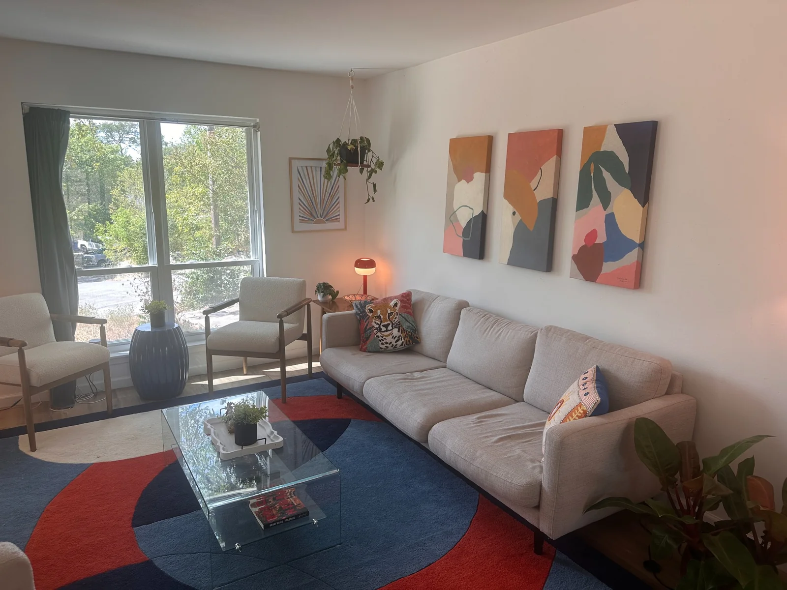 Living room with a gray sofa, colorful rug, abstract artwork, and a large window