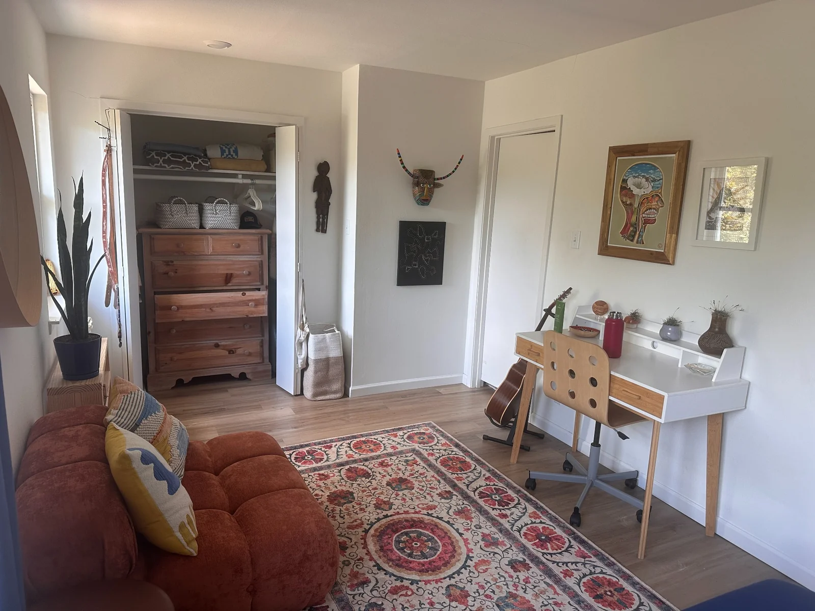 Sitting area at one end of a bedroom, with a white desk, rust-colored sofa, patterned rug, and closet